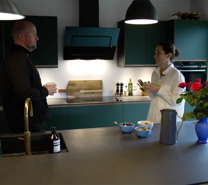 En mand og en kvinde står og taler sammen i et moderne køkken i et moderne hus. De står bag en køkken-ø.
