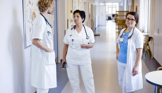 Tre hospitalsansatte 1 kvindelig overlæger og 2 yngre læger konverserer på en hospitalsgang