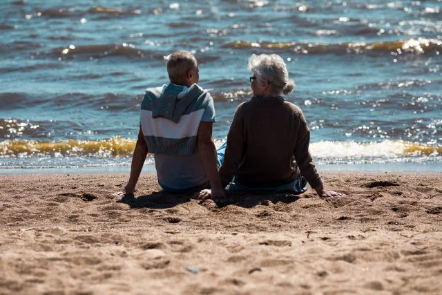To ældre personer der sidder på stranden og kigger ud over vandet - pension